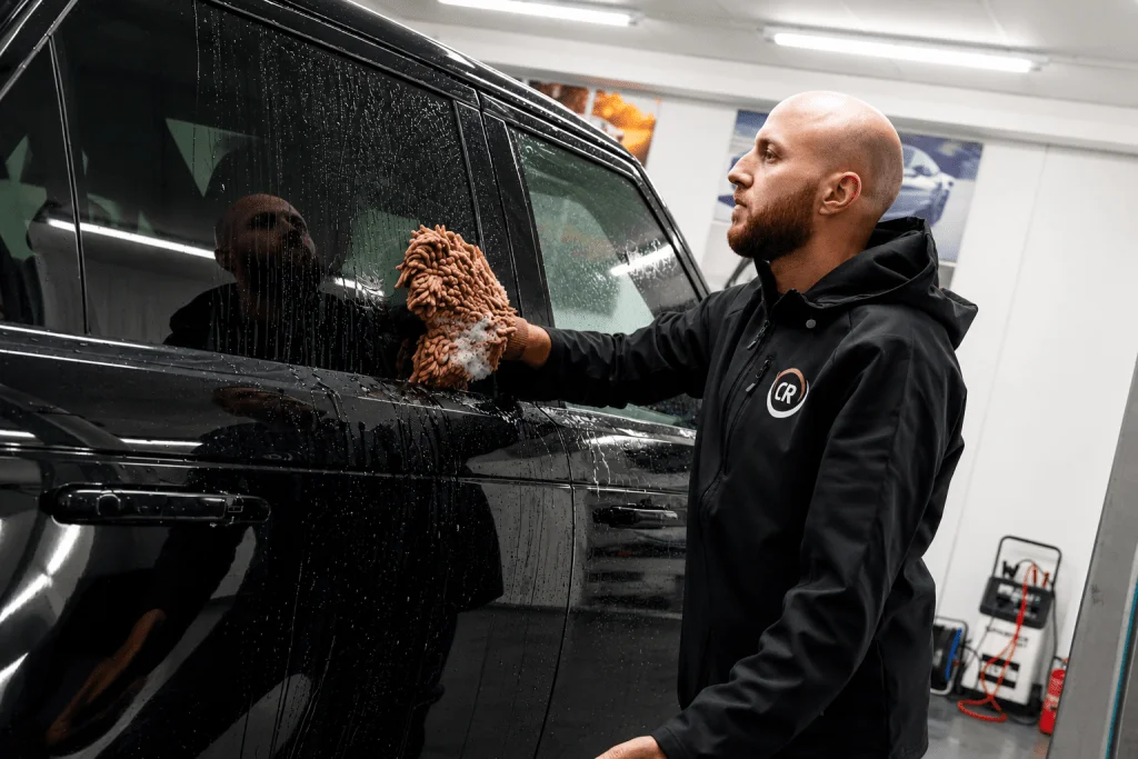 Medewerker reinigt een zwarte auto met een washandschoen
